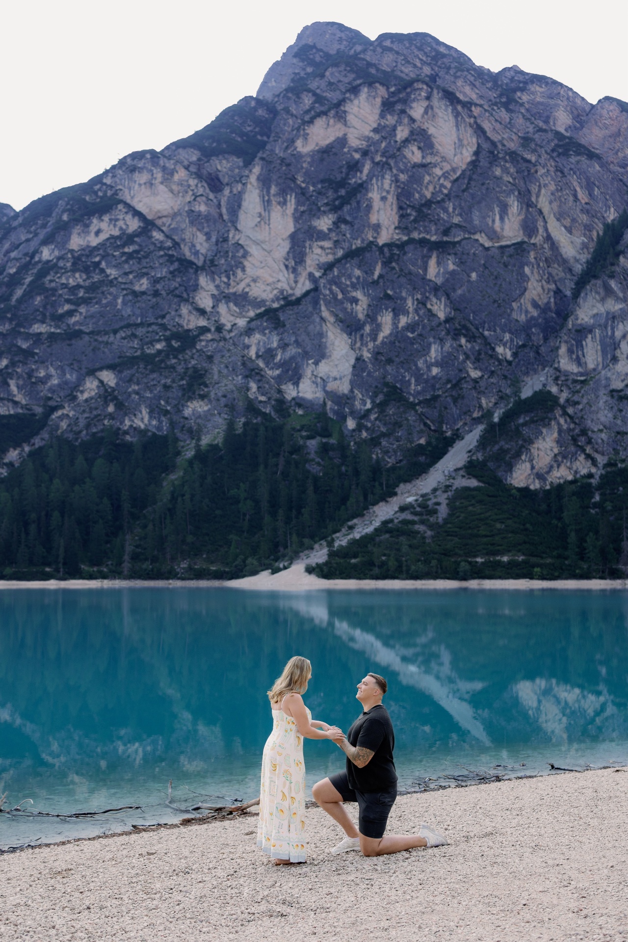 Jamie on one knee proposing to Victoria on the shore of Lago di Braies, the Dolomites rising behind them